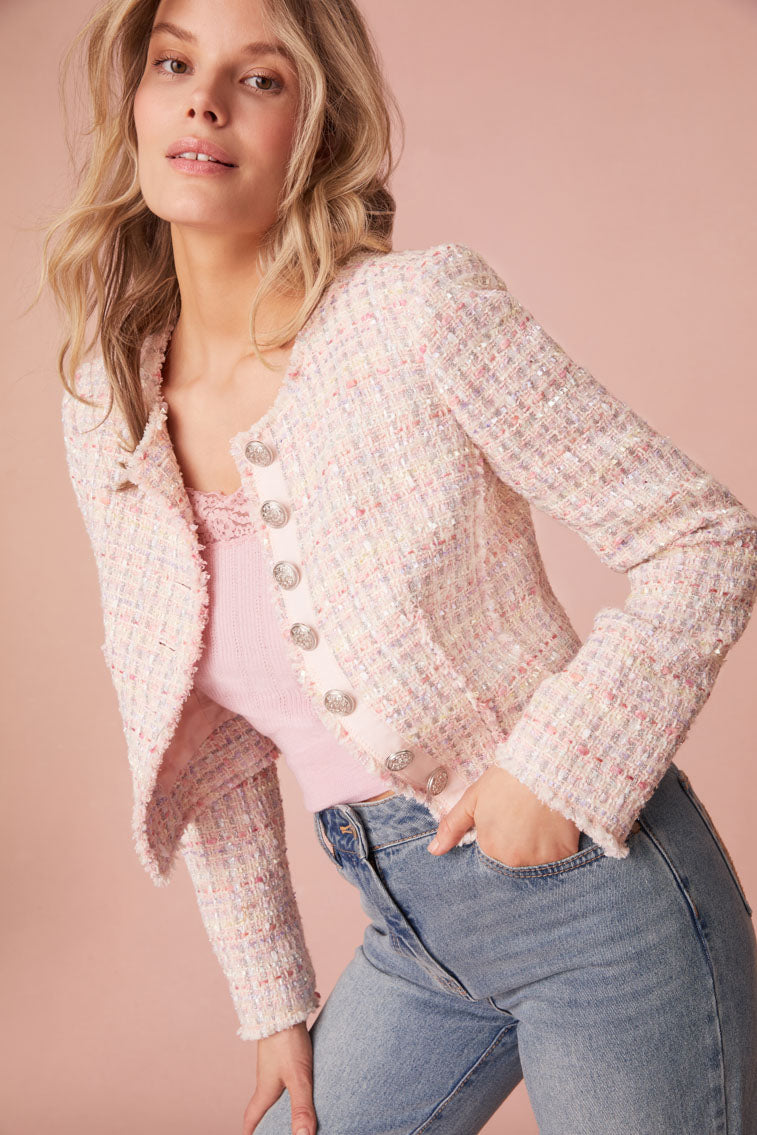 Pink and white tweed cropped jacket with shimmer details and a slim fit on the body. The sleeves fray at the edges and a custom silver LoveShackFancy logo military buttons down center front that descends to a cutout feature to finish the piece.