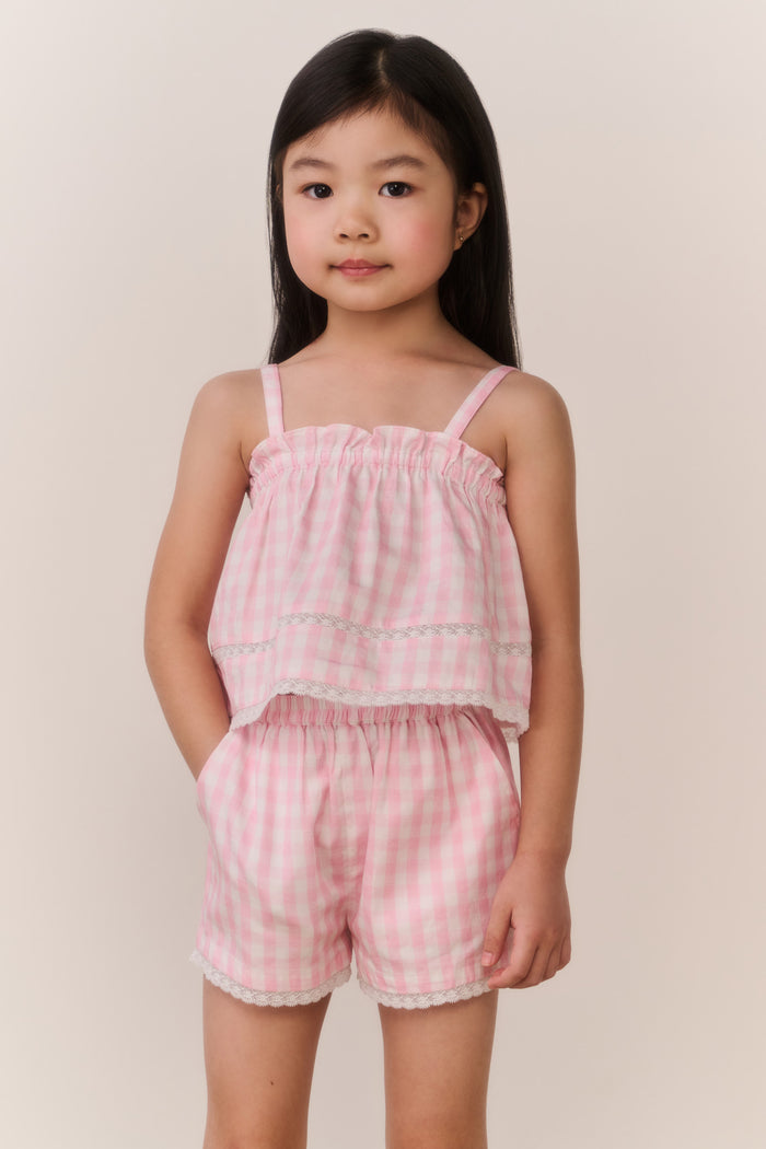 Young girl wearing a pink checkered outfit against a plain background