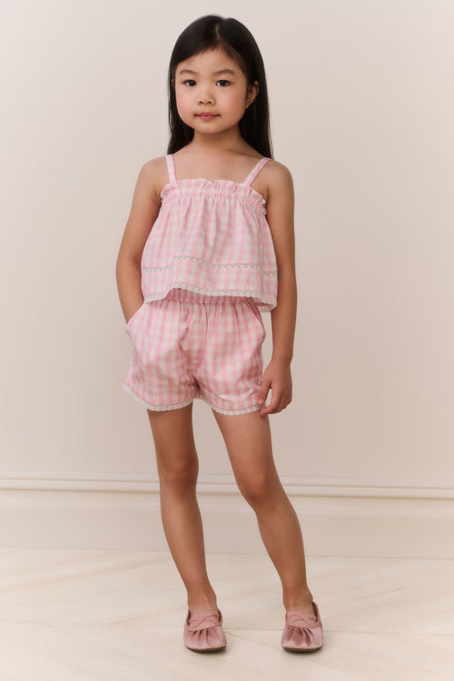 Young girl wearing a pink checkered outfit against a plain background