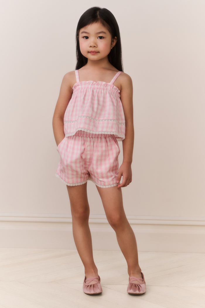 Young girl wearing a pink checkered outfit against a plain background