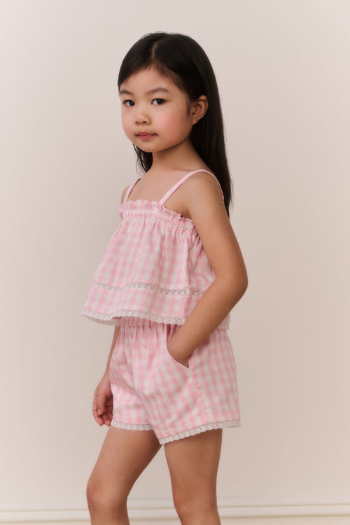 Young girl wearing a pink checkered outfit against a plain background