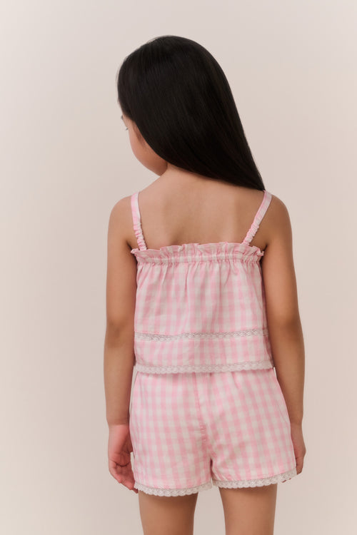 Young girl wearing a pink checkered outfit against a plain background