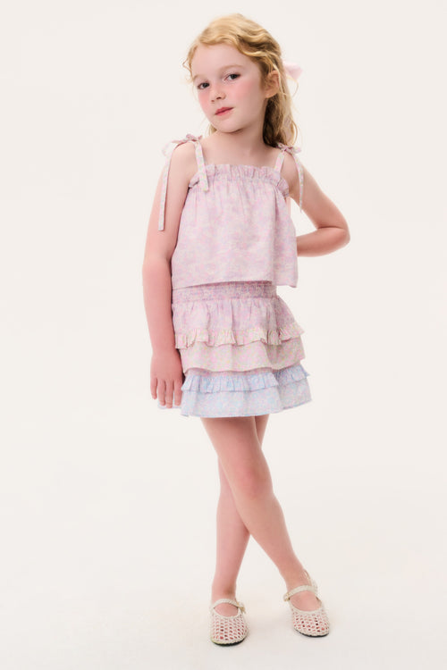 Young girl wearing a pink sleeveless top and matching skirt with ruffled layers on a white background