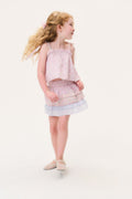 Young girl in a light pink skirt and matching sleeveless top with ruffled layers on a white background