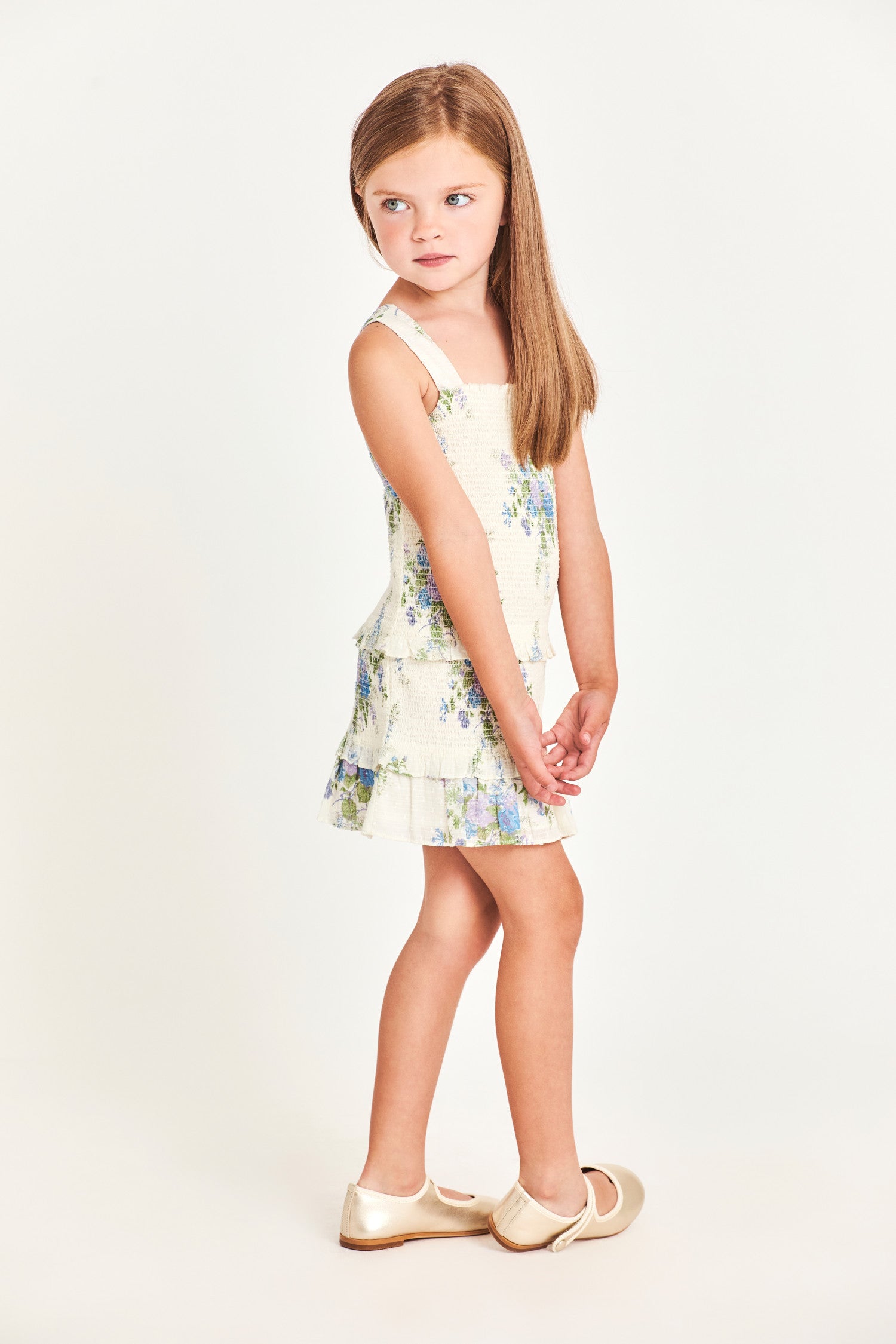 The girl’s Clancey dress is a white 100% cotton dress with blue flower detailing. It features a ruffled two-tier bottom and waistband. 