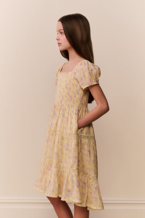 Young girl wearing a yellow floral dress against a beige background
