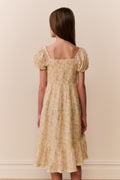 Woman wearing a yellow floral dress against a beige wall