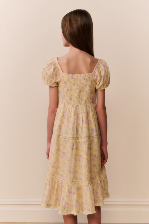 Woman wearing a yellow floral dress against a beige wall