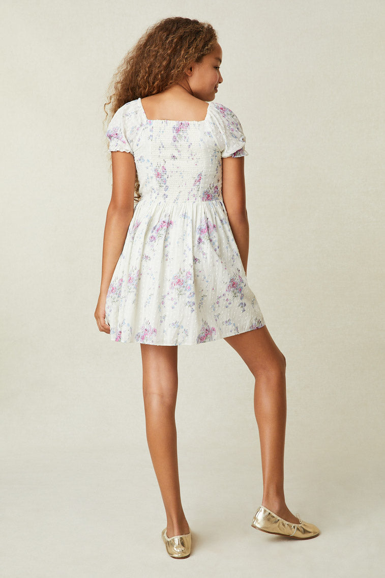 Back image of model wearing girl's white mini dress with purple and pink floral print.