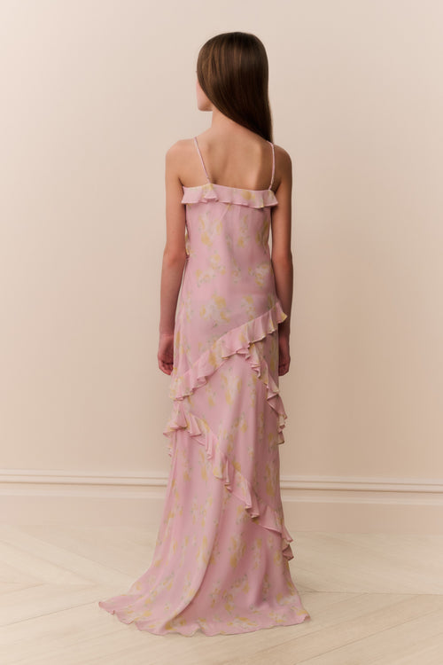 Girl wearing a pink floral dress with ruffled layers on a plain background