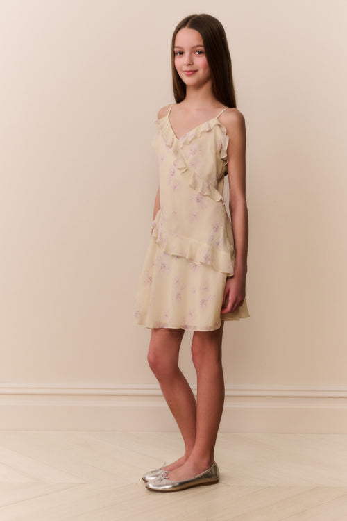 Woman wearing a light yellow dress with floral patterns against a beige background