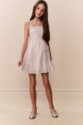 Girl wearing a white sleeveless lace dress against a plain background