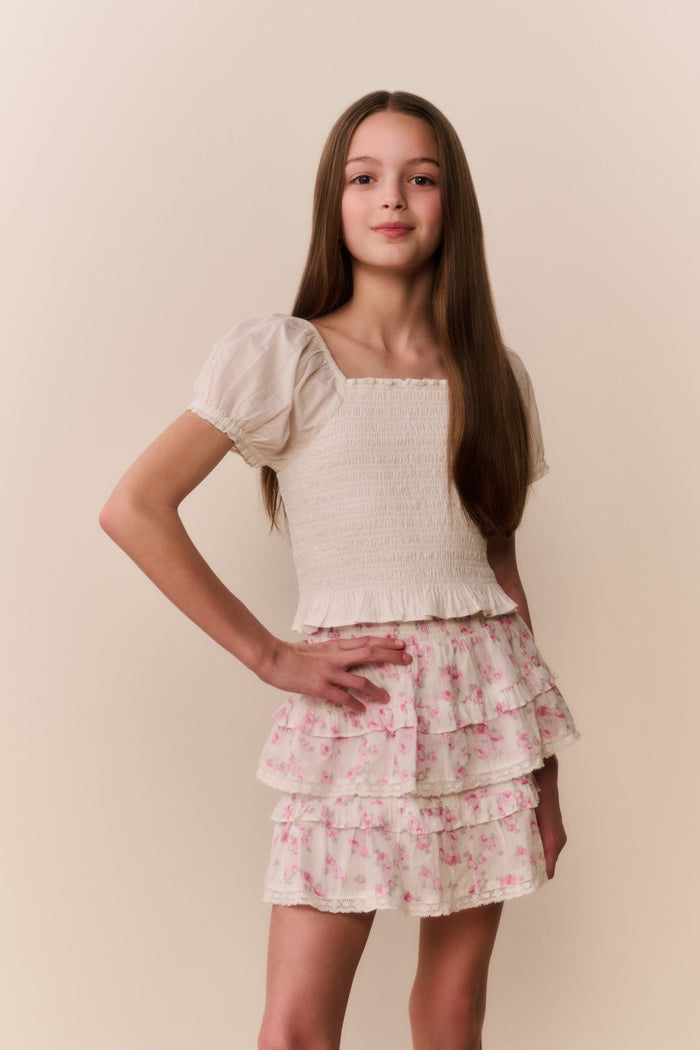 Girl wearing a white top and floral ruffle  skirt on a beige background