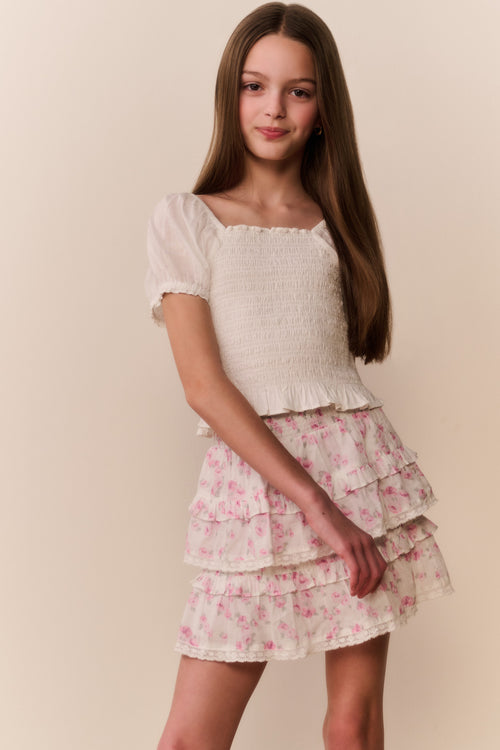 Girl wearing a white top and floral ruffle  skirt on a beige background