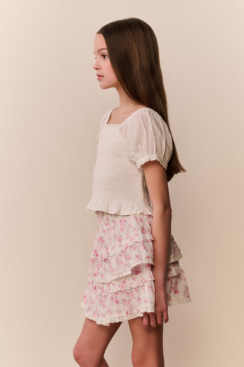 Girl wearing a white top and floral ruffle  skirt on a beige background