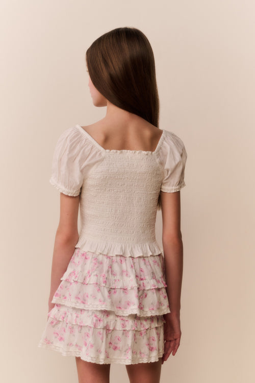 Girl wearing a white top and floral ruffle  skirt on a beige background