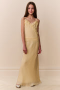 Girl wearing a light yellow sleeveless ruffle detail top and matching long skirt against a beige background