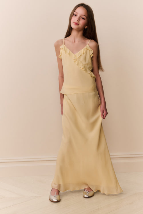 Girl wearing a light yellow sleeveless ruffle detail top and matching long skirt against a beige background