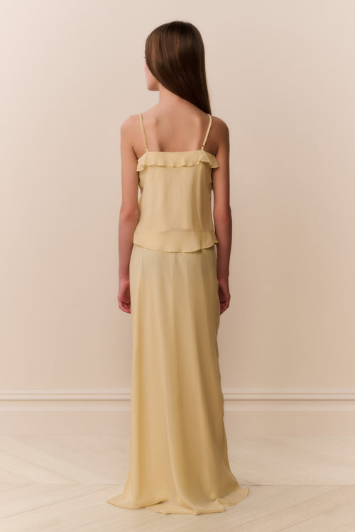 Girl wearing a light yellow top and matching long skirt against a beige background