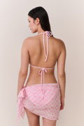 Woman wearing a pink bikini with a matching wrap coverup on a plain background