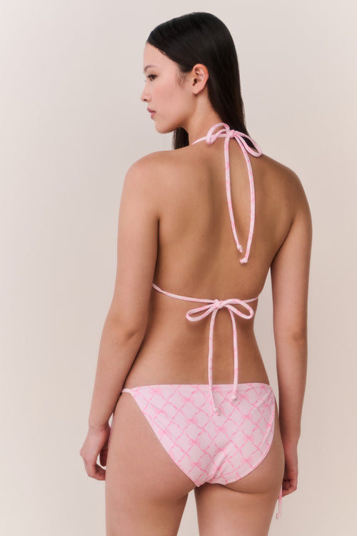 Woman wearing a pink bikini with a bow pattern on a beige background