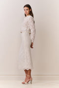 Woman wearing a white lace jacket and skirt outfit on a plain background
