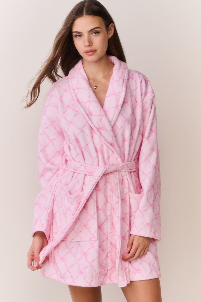Woman wearing a pink bow print robe against a plain background
