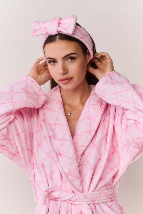 Woman wearing a pink bow print robe and headband against a light background