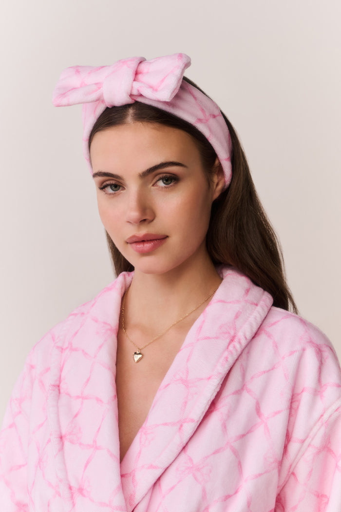 Woman wearing a pink bow print robe and headband against a light background