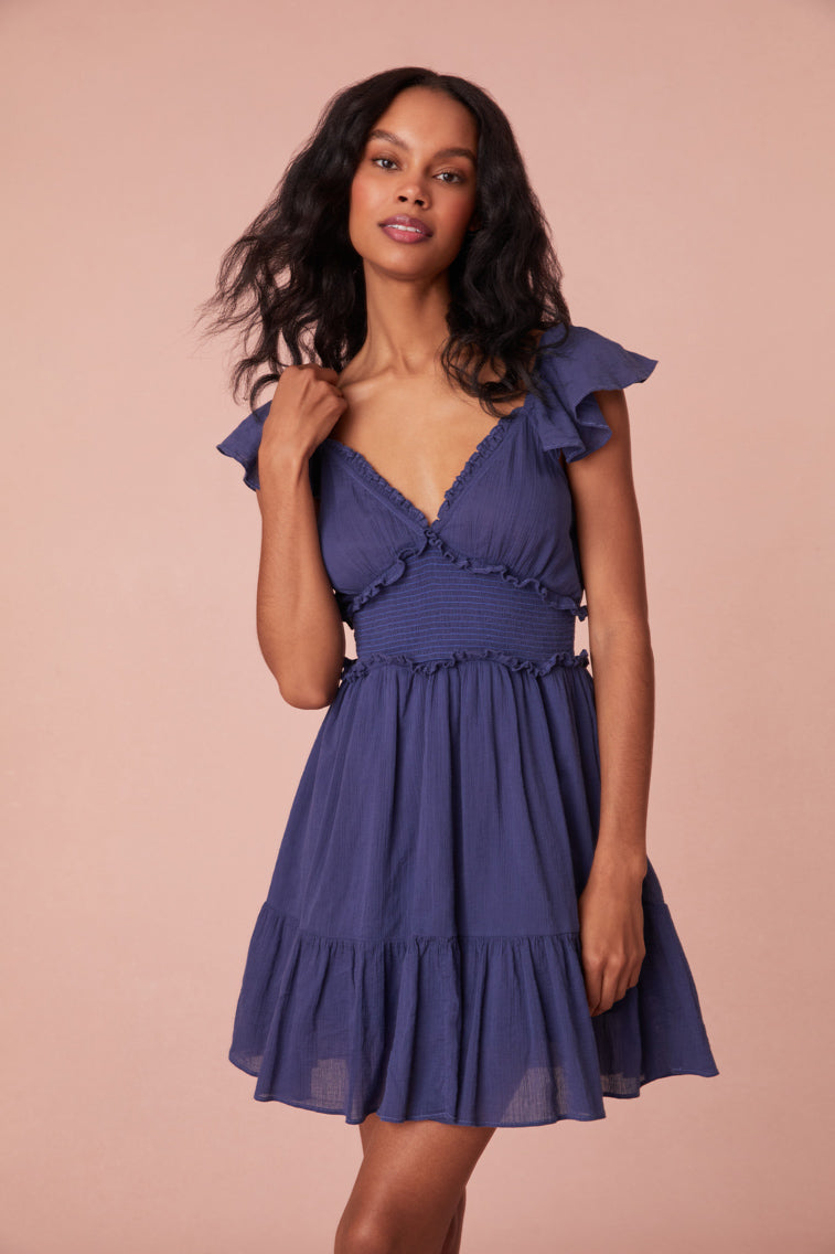 Mini dress featuring short flutter sleeves with cascading ruffles and elastication, a v-neckline, a smocked bodice with ruffles for a flattering silhouette, and a beautiful flouncy skirt.