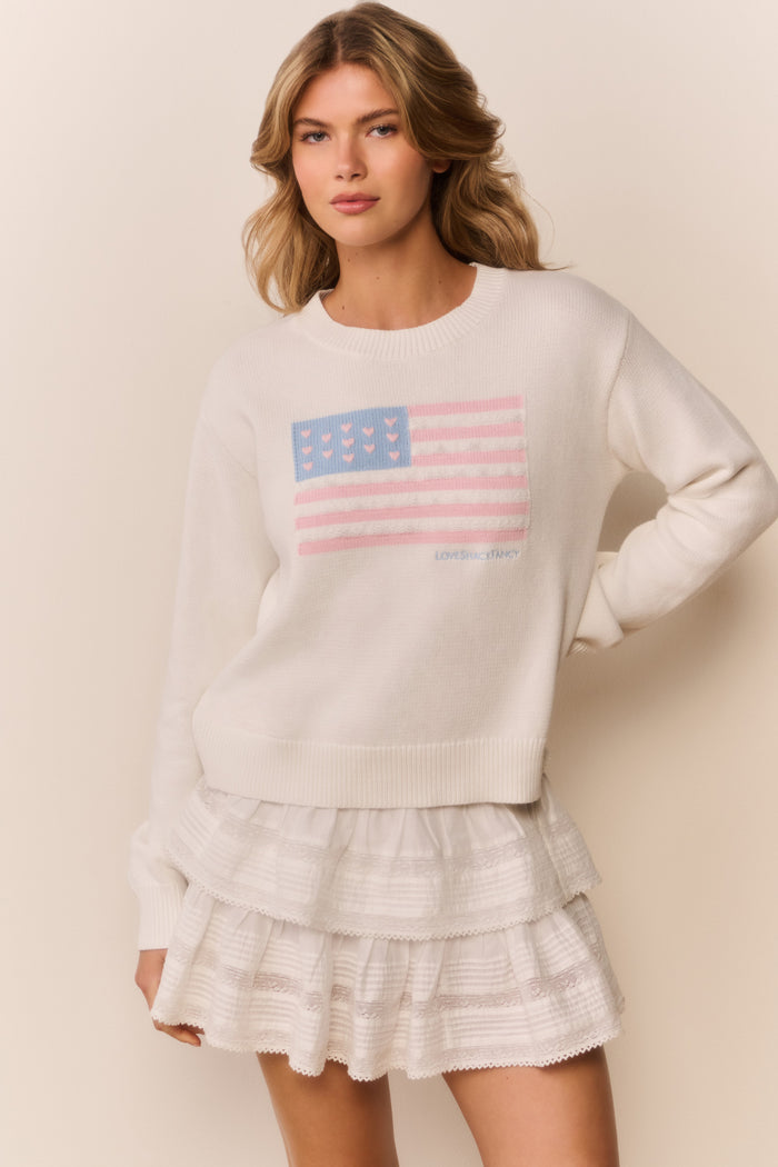 Woman wearing a white sweatshirt with an American flag design on a beige background