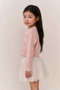 Young Girl wearing a pink sweater and white skirt lace against a plain background