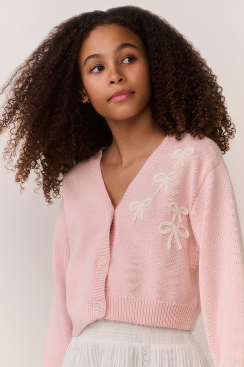 Tween wearing a pink sweater and white lace skirt on a plain background