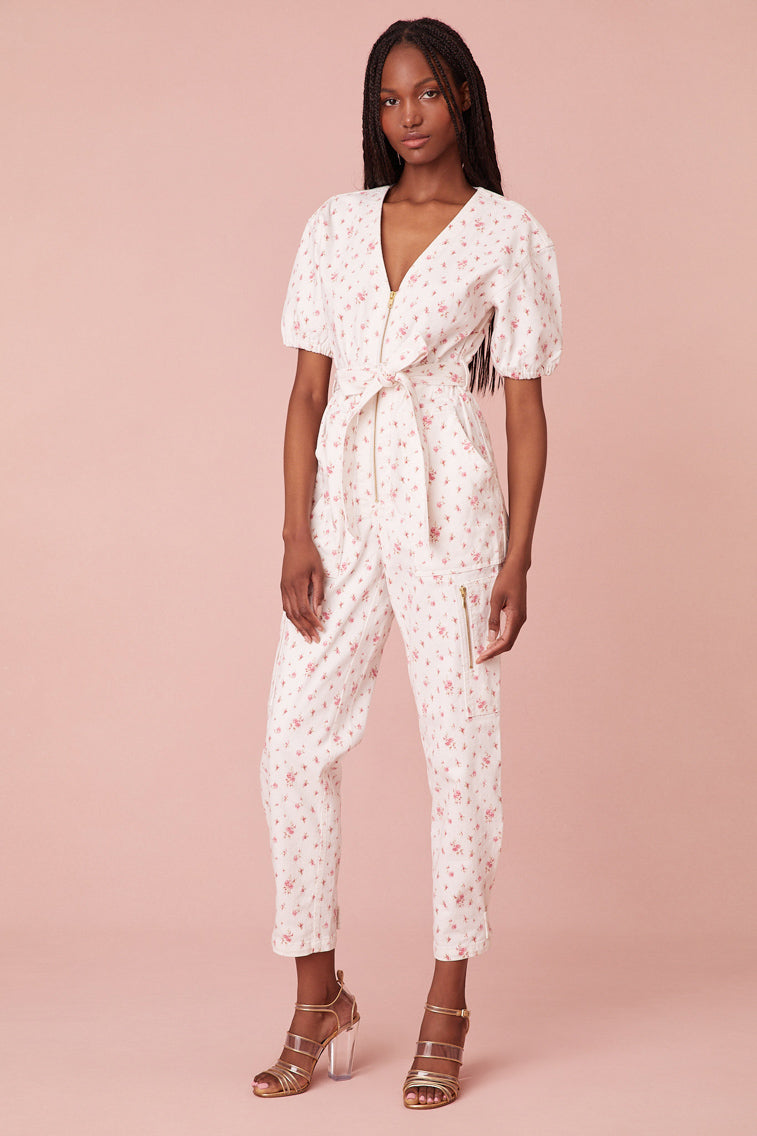 Jumpsuit featureing a slightly faded floral print on a stone-washed denim fabric. Features short puff sleeves, a v-neckline, cinching at the waist, elastic at the back, and a midi length. Includes a zipper at the front and a snap at the leg.