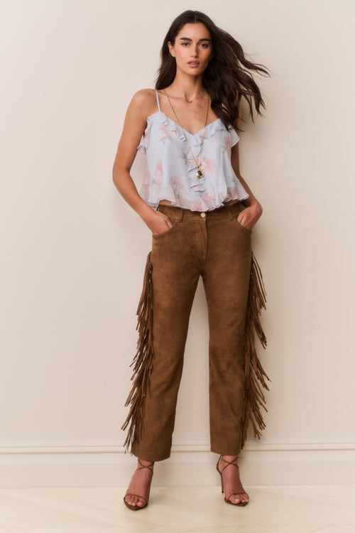 Woman wearing a blue floral top and brown fringed pants against a plain background
