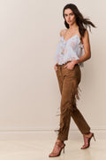 Woman wearing a light blue floral top and brown fringed pants against a plain background
