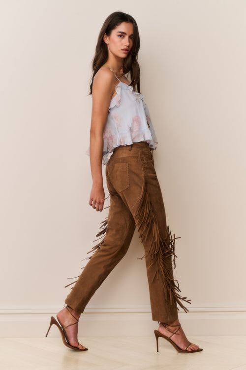Woman wearing a blue floral top and brown fringed pants on a plain background