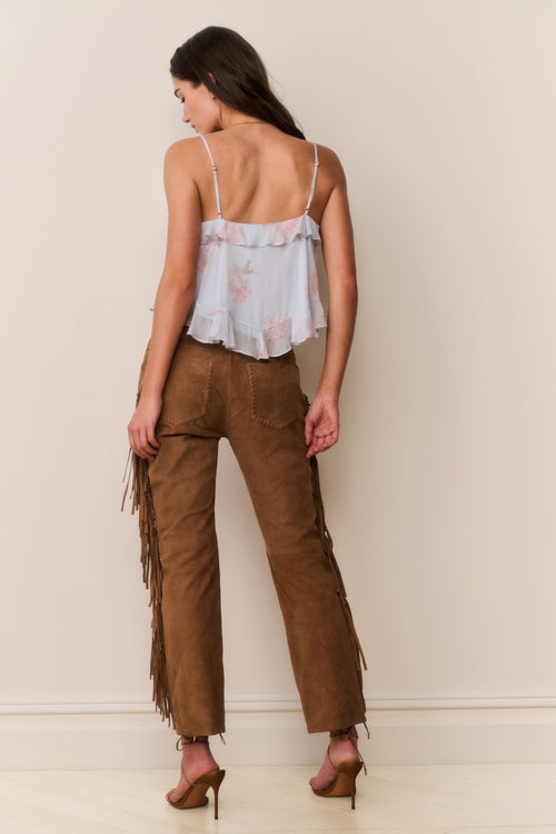 Woman wearing a light-colored top and brown fringed pants against a plain background