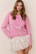 Woman wearing a pink sweater with a heart design and a white lace skirt against a beige background