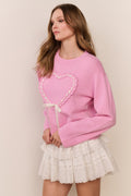 Woman wearing a pink sweater with a heart design and a white lace skirt on a beige background