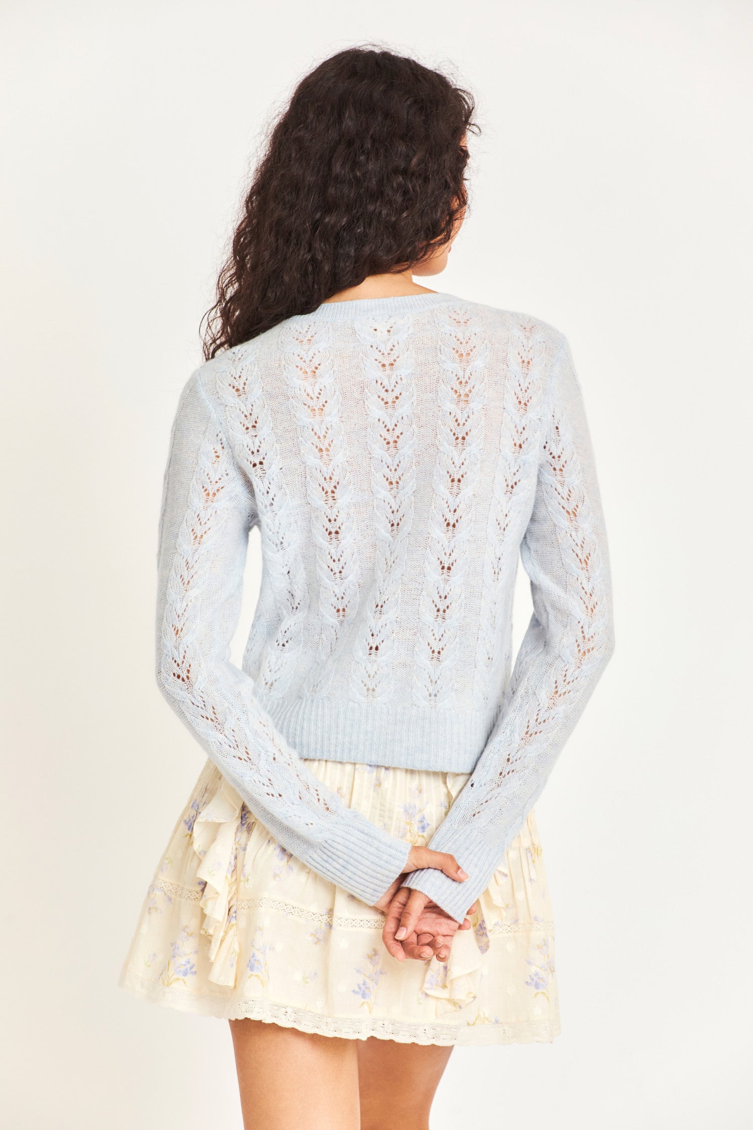 The lightweight baby blue cable knit sweater is a cashmere wool blended sheer fabric with pointelle detailing and a hand embellished neckline with crystals and clusters of iridescent pearls. 