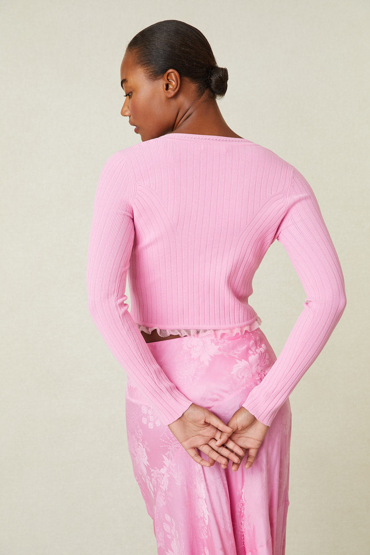 Back image of model wearing pink v-neck cardigan with ruffle detail at hem and button up closure.