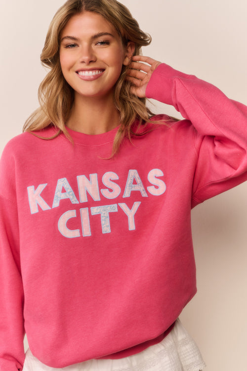 Woman wearing a pink sweatshirt with 'Kansas City' text on a plain background