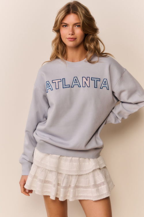 Woman wearing white mini skirt with ruffles and grey pullover that says Atlanta across the front