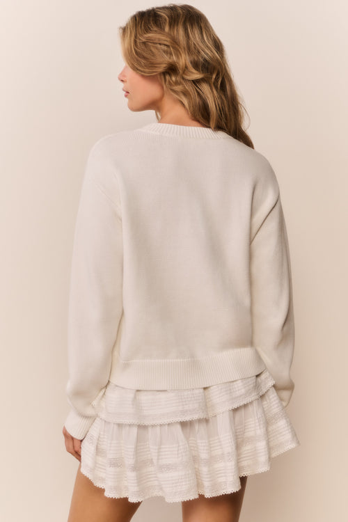 Woman wearing a cream-colored sweater and ruffled skirt against a beige background