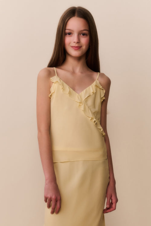 Young girl wearing a yellow top and matching skirt with ruffled details on a beige background