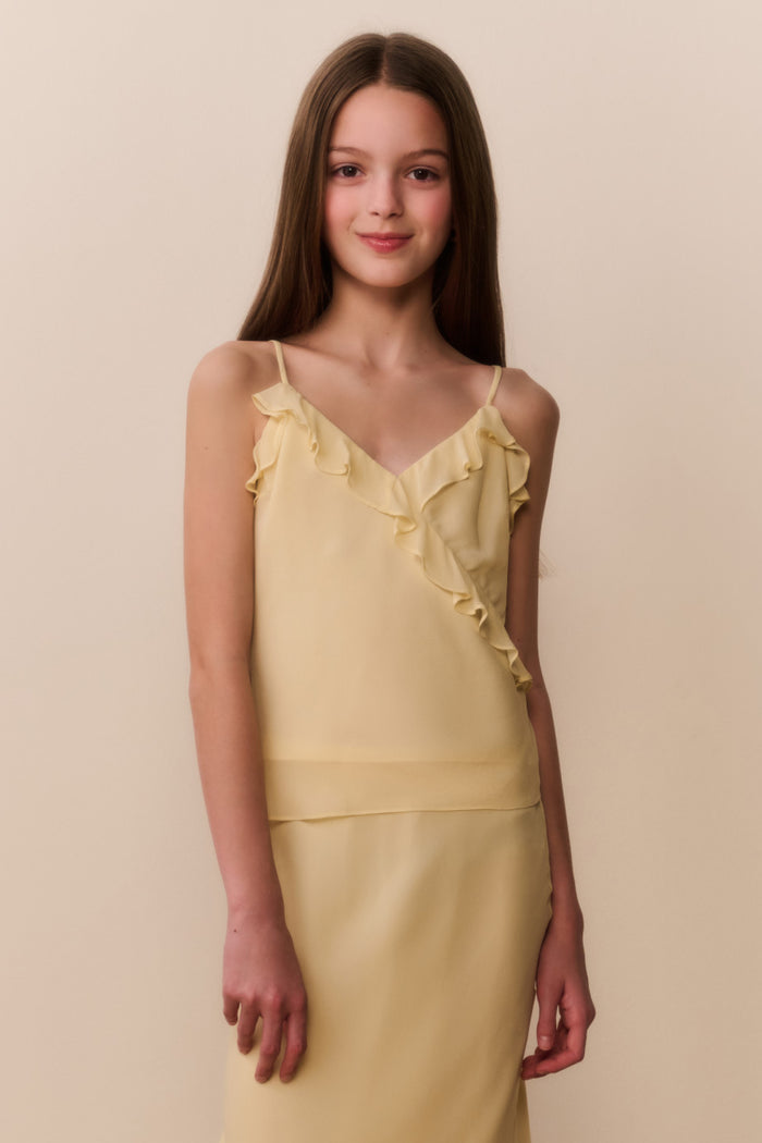 Young girl wearing a yellow top and matching skirt with ruffled details on a beige background