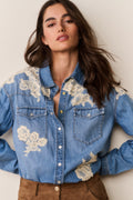 Woman wearing Blue denim shirt with floral lace embroidery and suede brown pants on a beige background