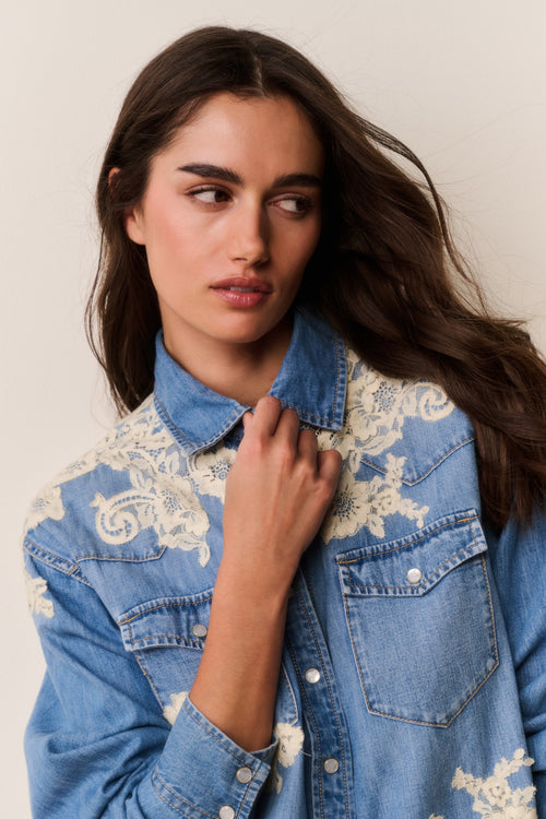 Woman wearing Blue denim shirt with floral lace embroidery on a beige background