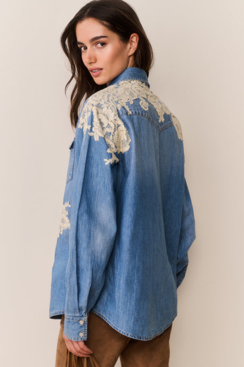 Woman wearing Blue denim shirt with floral lace embroidery on a beige background